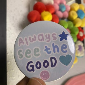 May include: A blue button with the text "Always see the good" in colourful letters. The button also features a blue star, a blue heart, and a smiley face.