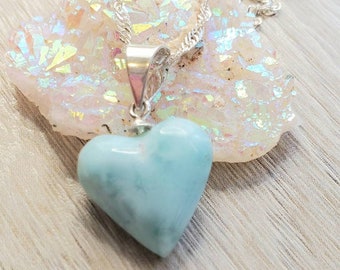 May include: A silver chain necklace with a light blue heart-shaped pendant. The pendant is made of a natural stone with a marbled pattern.