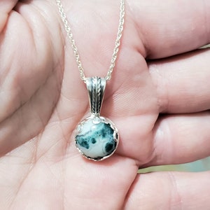 May include: A silver chain necklace with a round pendant featuring a green and white agate stone.