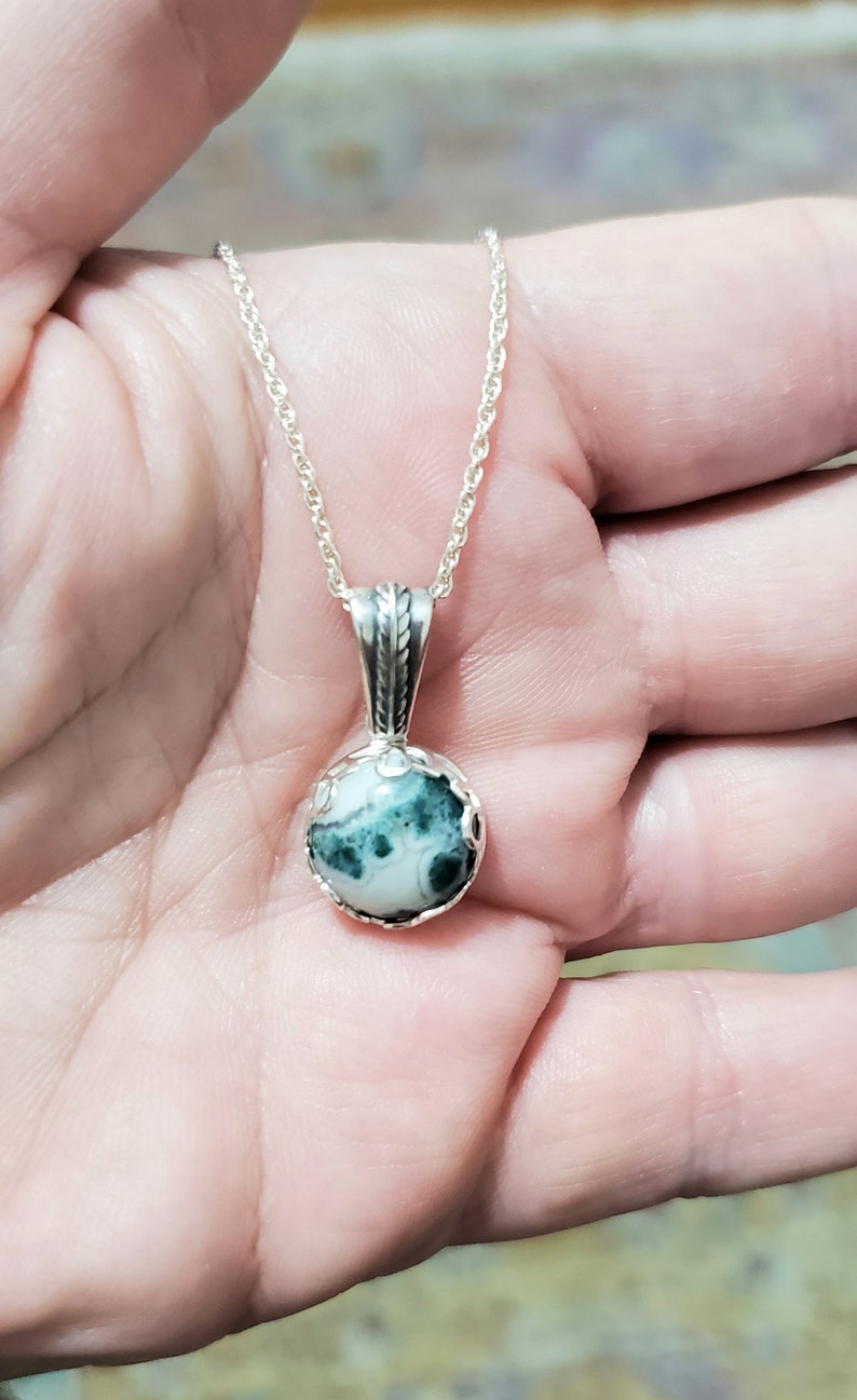 May include: A silver chain necklace with a round pendant featuring a green and white agate stone.