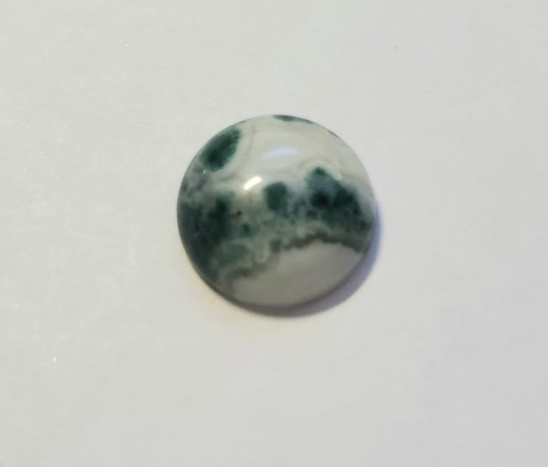 May include: A round, green and white agate cabochon with a swirling pattern.