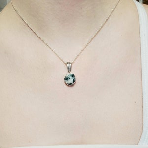 May include: A silver chain necklace with a round pendant featuring a green and white stone.