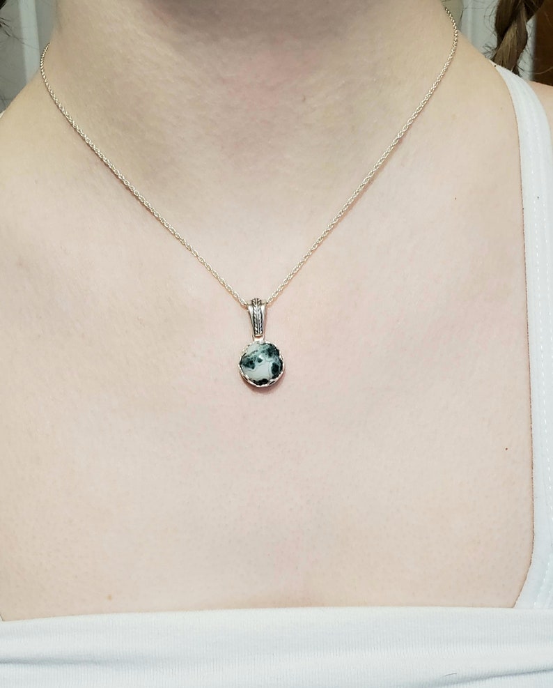 May include: A silver chain necklace with a round pendant featuring a green and white stone.