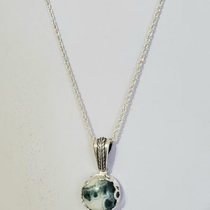 May include: A silver chain necklace with a green and white agate pendant. The pendant is set in a silver bezel and has a rope-like design around the edge.