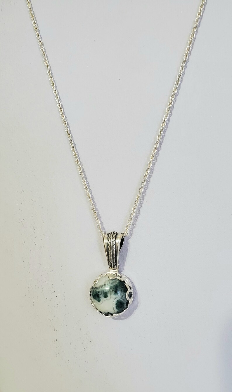 May include: A silver chain necklace with a green and white agate pendant. The pendant is set in a silver bezel and has a rope-like design around the edge.
