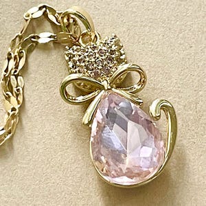 Sparkling Gold Tone Pink Jewel Cat with White Rhinestone Encrusted Face and Cute Gold Bow Wrapped Around the Neck on Gold Plated 18&quot; Chain