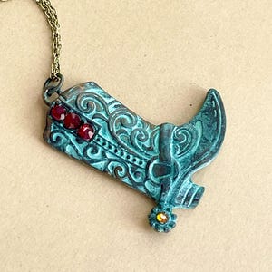 May include: A turquoise blue metal cowboy boot pendant necklace with red and yellow rhinestones.