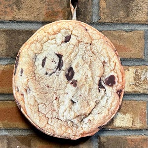 May include: A round, brown and white pot holder with a cookie design. The pot holder has a loop for hanging.