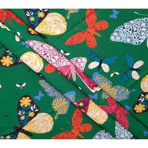 May include: Green fabric with a repeating pattern of colorful butterflies, bees, and small blue butterflies. The butterflies feature orange, yellow, white, and blue wings. The fabric is folded, showing the pattern at different angles.