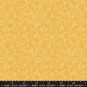 May include: Mustard yellow fabric with a repeating pattern of overlapping, freeform, light tan and off-white circles. The fabric has a modern, abstract design. The bottom of the fabric has the text "RUBY STAR SOCIETY".