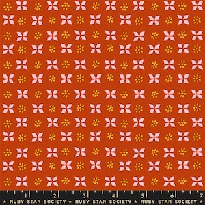 May include: A fabric with a repeating pattern of white diamond shapes and yellow flower-like designs on a rust-colored background. The fabric has a ruler at the bottom with the text "RUBY STAR SOCIETY".
