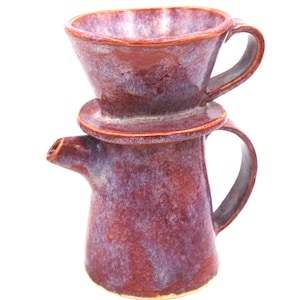 May include: A ceramic pour-over coffee dripper stacked on top of a matching ceramic pitcher. Both pieces feature a mottled, variegated glaze in shades of deep reddish-purple and violet with a smooth, glossy finish and curved handles.