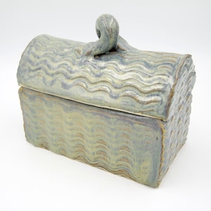 May include: A ceramic box with a lid, featuring a wavy pattern and a curled handle. The box is primarily green and blue, with brown accents. The rectangular box is approximately 8 inches long, 5 inches wide, and 4 inches tall.
