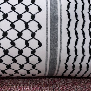 May include: A white and black patterned fabric with a geometric design. The fabric has a black and white striped border.