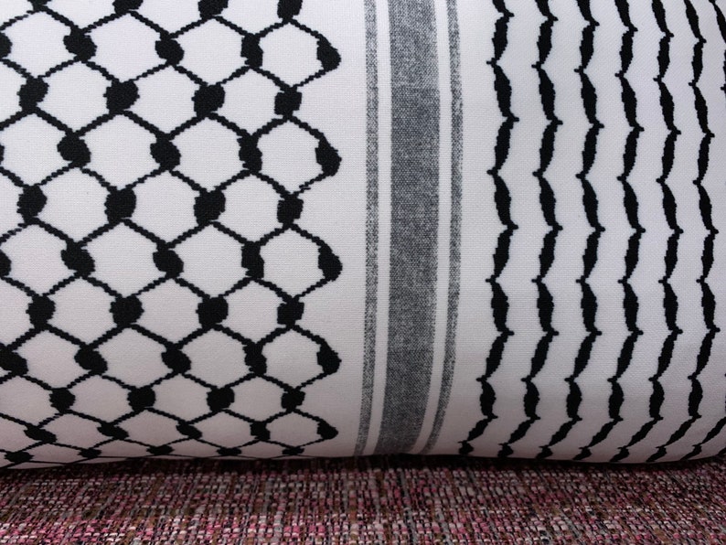 May include: A white and black patterned fabric with a geometric design. The fabric has a black and white striped border.