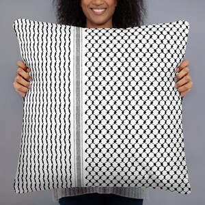 May include: A white and black patterned throw pillow with a geometric design. The pillow is being held by a person.