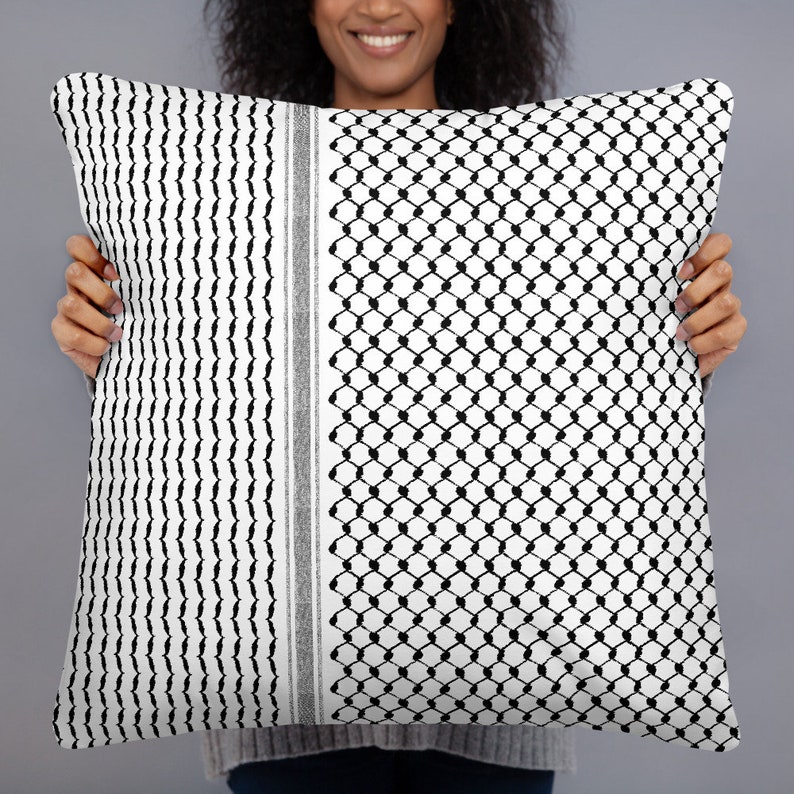 May include: A white and black patterned throw pillow with a geometric design. The pillow is being held by a person.