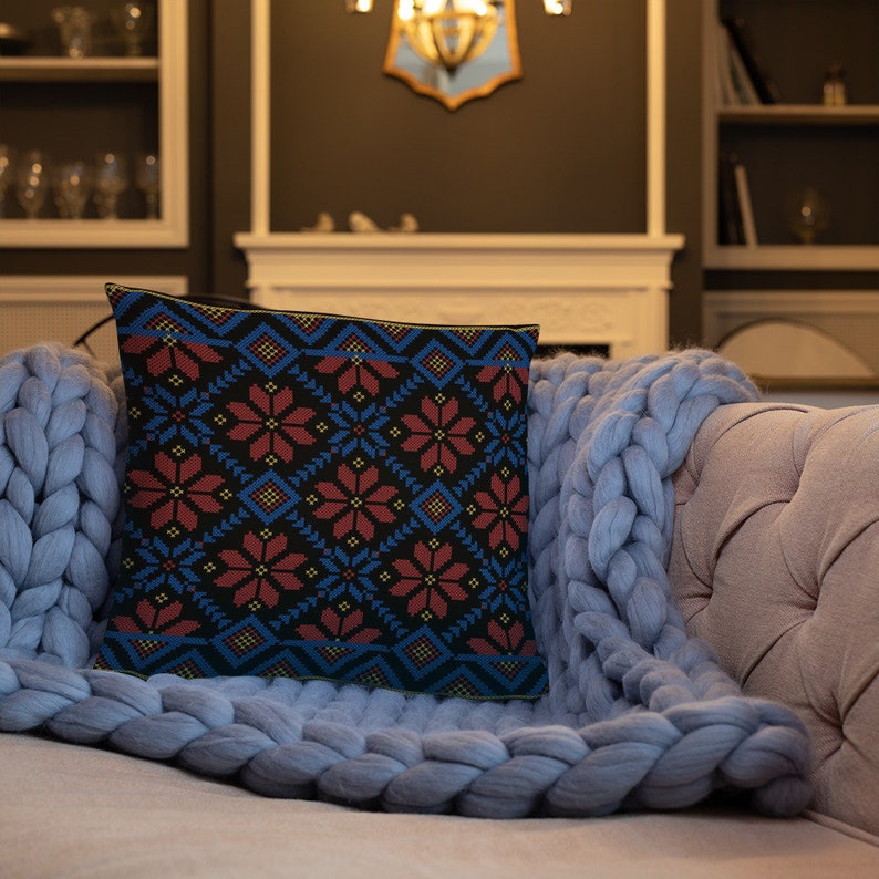 Pu&ograve; includere: Un cuscino con un motivo geometrico blu e rosso. Il cuscino &egrave; su una coperta di maglia blu chiaro su un divano.