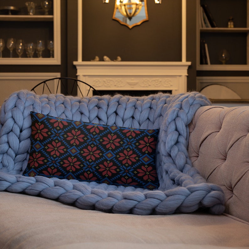 Pu&ograve; includere: Un divano color grigio chiaro con una coperta blu e un cuscino con un motivo. Il cuscino ha uno sfondo nero con motivi geometrici rossi e blu.
