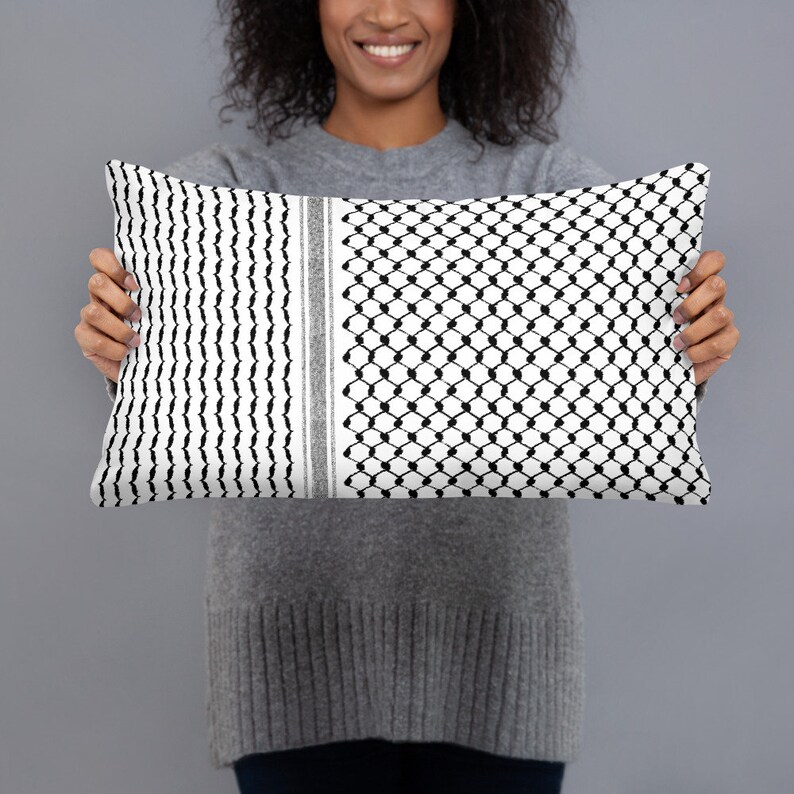 May include: A white and black patterned throw pillow with a geometric design. The pillow is being held by a person.