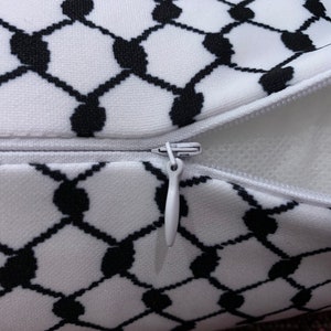 May include: A white pillow with a black and white geometric pattern. The pillow has a zipper closure and is filled with white stuffing.