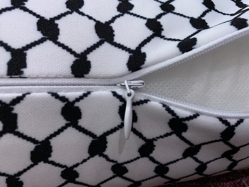 May include: A white pillow with a black and white geometric pattern. The pillow has a zipper closure and is filled with white stuffing.