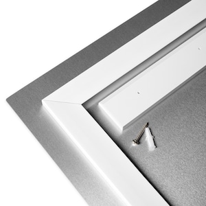 May include: Close-up of a white metal frame with a white plastic mounting bracket and a screw and plastic anchor. The frame is attached to a silver metal surface.