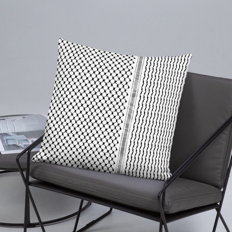 May include: A black and white patterned throw pillow with a geometric design. The pillow is on a gray chair with black metal legs.