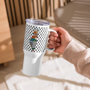 May include: White travel mug with a black and white patterned design featuring a colorful outline of the country of Palestine. The mug has a lid and a handle.