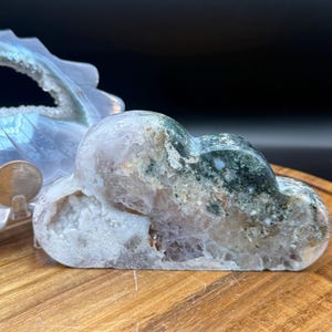 Puede incluir: Escultura de cristal con forma de nube, con una mezcla de colores blanco, verde y marrón. El cristal tiene un centro hueco y está sobre una superficie de madera. Es un objeto decorativo.