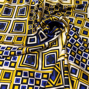 May include: A close-up of a silk fabric with a geometric pattern. The design features squares and diamonds in yellow, blue, black, and white. The fabric is draped, showing the texture and flow of the material. The overall theme is a modern, abstract design.