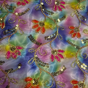 以下が含まれることがあります： 青、紫、ピンク、黄色の色合いのタイダイ効果のある鮮やかな生地。 金色のスパンコールで飾られた花のつるが、赤とピンクの花とともに表面に刺繍されています。 生地は光沢があり、絹のような外観をしています。