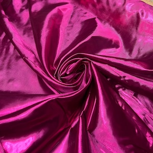 May include: A close-up of a vibrant magenta fabric with a glossy, reflective surface. The fabric is artfully arranged in a spiral, showcasing its flowing texture and sheen. The material appears to be lightweight and suitable for various craft projects.
