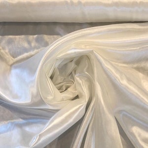 May include: White satin fabric with a smooth, silky texture. The fabric is folded and draped, showcasing its sheen and drape.