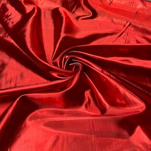 May include: A close-up of a vibrant red fabric with a glossy, reflective surface. The material is gathered and swirled, creating deep shadows and highlights. The fabric appears to be lightweight and flowing, suitable for apparel or decorative use.