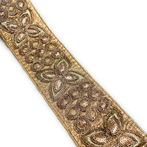 May include: Gold-colored decorative ribbon with intricate floral and circular patterns. The ribbon features embroidered details with sequins and beads, creating a textured and ornate design. The ribbon is ideal for embellishing garments or craft projects.