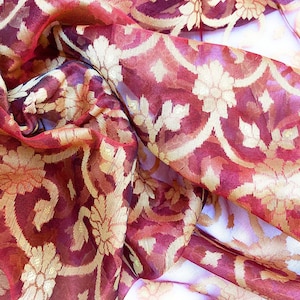 Pode incluir: Tecido vermelho transparente com um padrão floral dourado. O tecido está drapeado e dobrado, mostrando os detalhes intrincados do design.