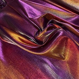 Puede incluir: Primer plano de tela iridiscente con brillo metálico. La tela hace la transición de un púrpura profundo a tonos vibrantes de naranja y rojo. El material está drapeado, creando pliegues y sombras que realzan las variaciones de color.