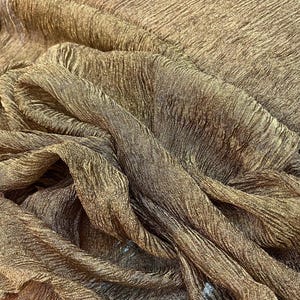 Può includere: Primo piano di un tessuto strutturato nei toni del marrone e dell'oro. Il tessuto ha un aspetto stropicciato, con creste e pieghe visibili. Il materiale appare morbido e fluido, con una sottile lucentezza. L'effetto complessivo è di lusso e profondità.