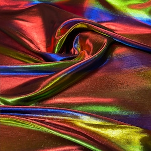 May include: Close-up of iridescent fabric with a metallic sheen. The fabric is folded and draped, showing off its shimmering colors of red, green, blue, and gold.