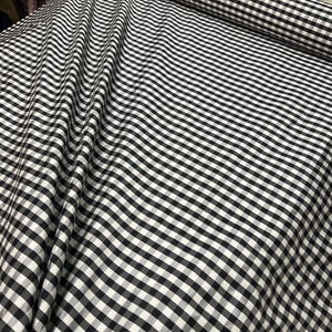May include: Black and white gingham fabric with a small check pattern. The fabric is folded and has a slight wave.
