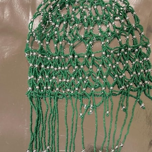 Puede incluir: Un tocado de cuentas verdes con detalles plateados. El intrincado diseño en forma de red presenta pequeñas cuentas verdes y cuentas plateadas. Largas hebras de cuentas verdes cuelgan de la parte inferior del tocado.