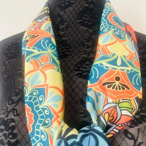 May include: A colorful scarf with a repeating floral pattern in shades of blue, orange, yellow, and green. The scarf is draped around a black form, showcasing its vibrant design and intricate details.