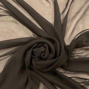 May include: A sheer black fabric draped into a central spiral formation. The material is translucent, creating layered shadows and varying depths of black tones throughout the folds as it radiates outward from the center point.
