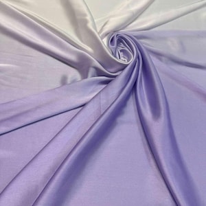 May include: A close-up shot of a fabric with a gradient effect. The fabric transitions from white to a soft lavender hue. The material is smooth and appears to be satin or silk, with folds and a swirled center.