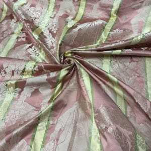 May include: A close-up of a pink and green fabric with a floral and figure pattern. The fabric has vertical green stripes and is gathered in a swirl. The fabric has a satin sheen.
