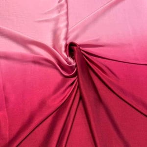 May include: A close-up of a fabric with a gradient of pink and red hues. The fabric is draped and folded, creating a textured effect. The colors transition smoothly from light pink to deep red.