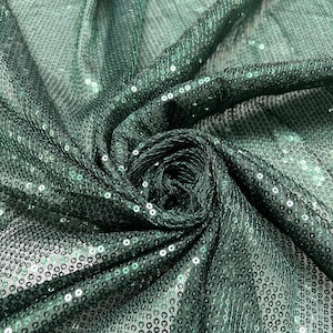 以下が含まれることがあります： 濃い緑色のスパンコール生地のクローズアップ。生地は折りたたまれ、ドレープされており、キラキラ光るスパンコールが映し出されています。スパンコールは密集しており、テクスチャのある表面を作り出しています。生地はわずかに光沢があります。