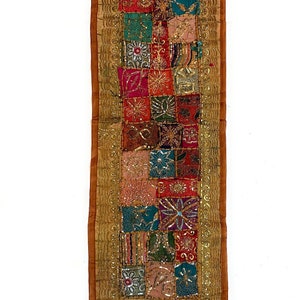 May include: A rectangular, colorful patchwork textile with a gold border. The patchwork features squares of red, green, pink, and blue fabric with embroidered floral and geometric designs. The border is a gold-colored fabric with a beaded trim.