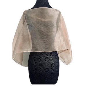 May include: A sheer, champagne-coloured capelet with a wide, boat-neck style opening and a lightweight, semi-transparent fabric that drapes over the shoulders. The garment features a subtle sheen and a structured, flared silhouette that falls evenly.
